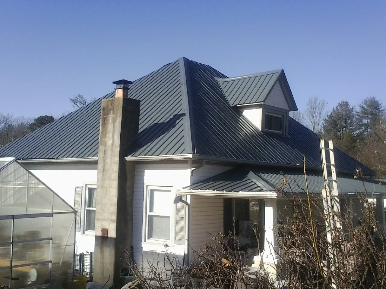 Dark blue standing seam metal roof on a white farmhouse with dormer — Slate & Tile Roof Repair by Roofing Brothers in Sour Lake