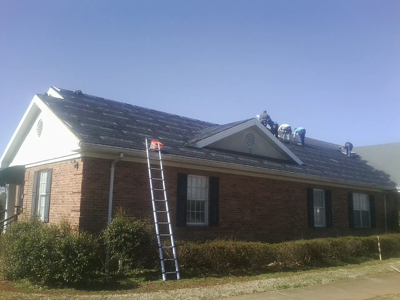 Crew tearing shingles off a brick ranch roof with a ladder set — Emergency Roof Repair work by our crew in Sour Lake