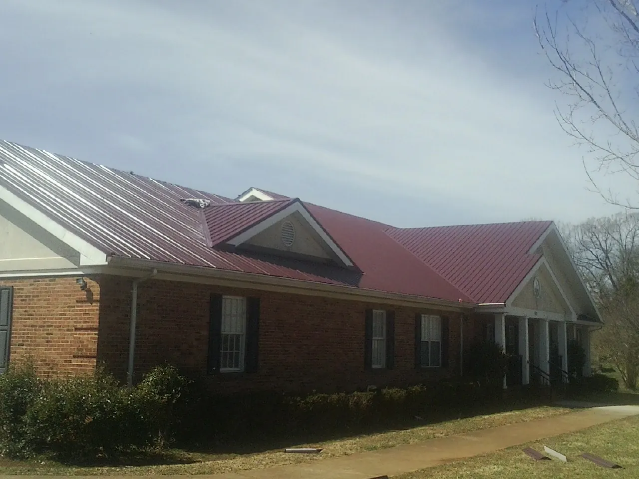 Red metal roof with gabled entries on a long brick building, from a Hail Damage Roof Repair job in Sour Lake