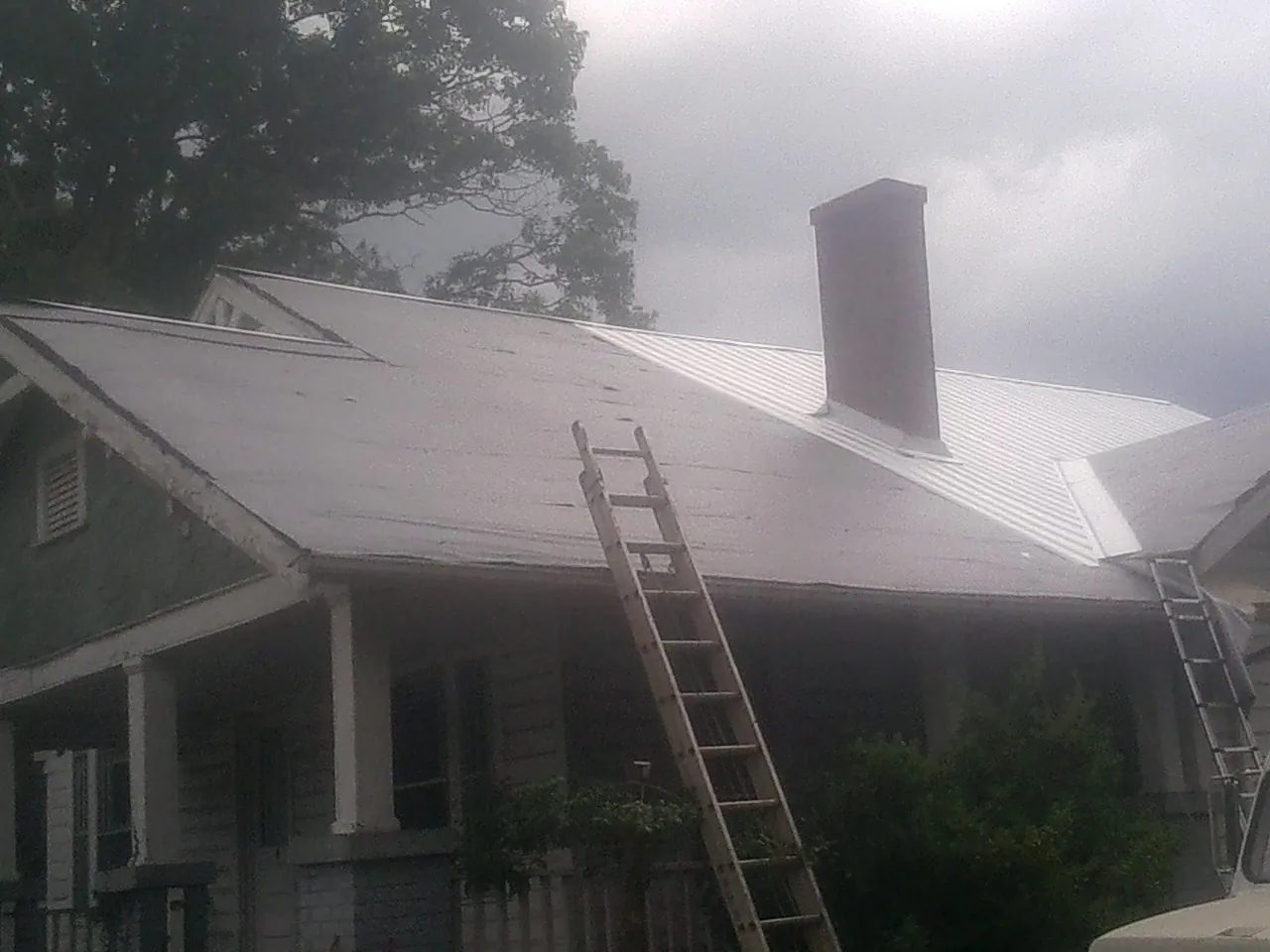 Ladders against a metal roof on an older home with a brick chimney in Sour Lake