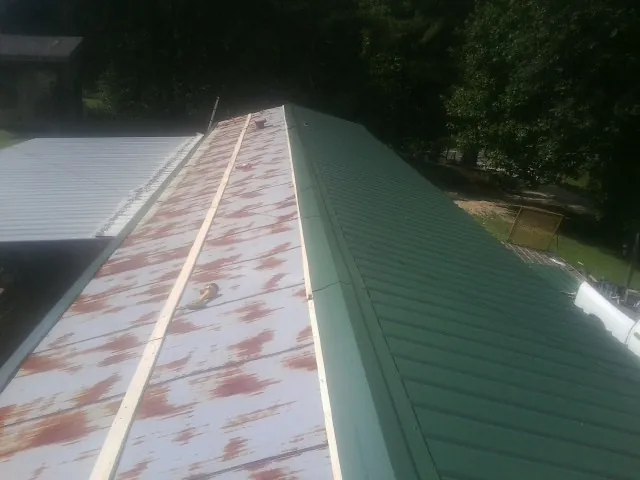 Old rusted panels beside newly installed green metal roofing — Wind Damage Roof Repair by Roofing Brothers in Sour Lake