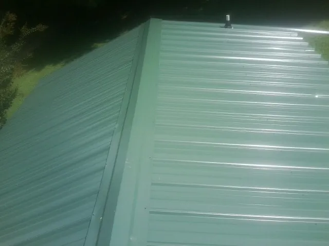New green metal panels meeting at the ridge of a roof — Flat Roof Repair work by our crew in Sour Lake