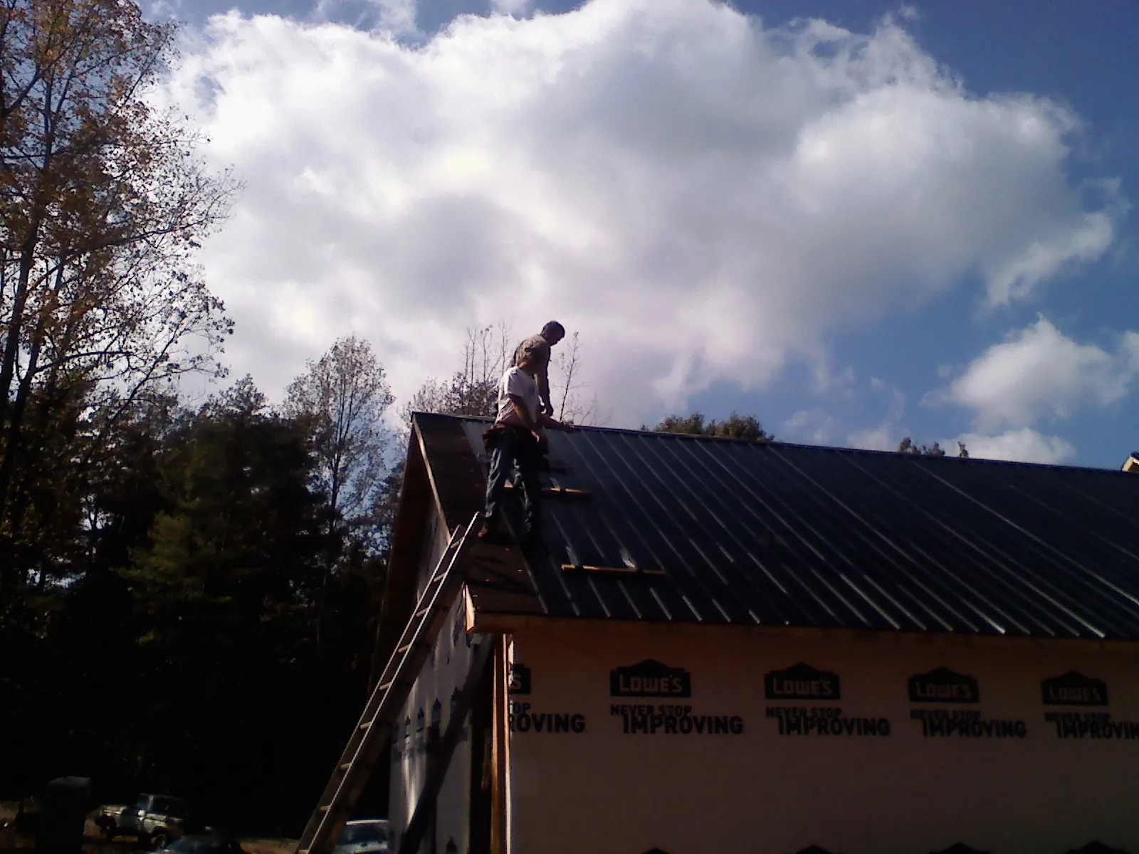 Roofer fastening dark metal panels high against a cloudy sky, from a Roof Inspection job in Sour Lake