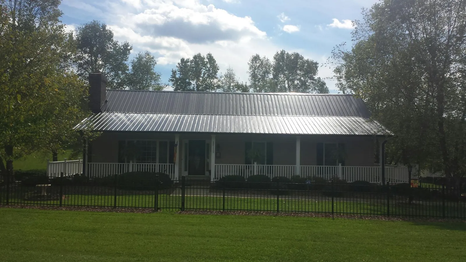 Gray metal roof on a brick ranch with a full width front porch — Gutter Guard Installation work by our crew in Sour Lake