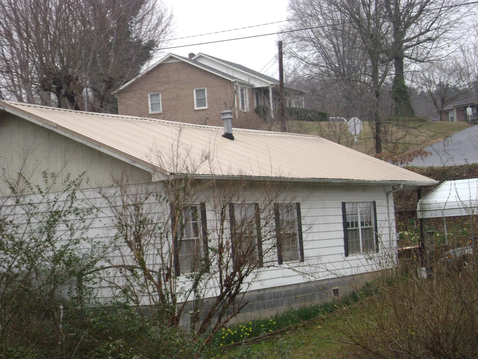 Tan metal roof on a white sided house set into a hillside — Commercial Roofing by Roofing Brothers in Sour Lake