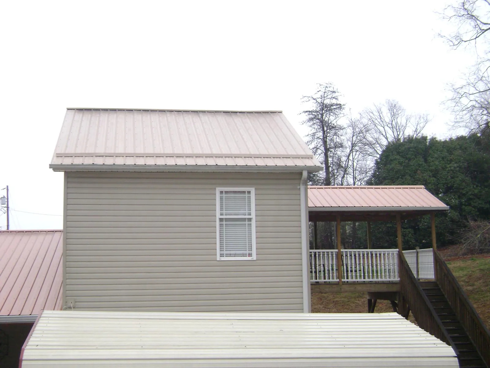 Tan metal roofs on a two story addition and attached porch, from a Roof Replacement job in Sour Lake