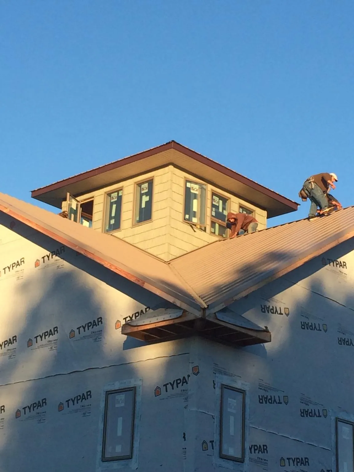 Roofers working around a rooftop cupola on a new metal roof at sunset — Roof Waterproofing in Sour Lake by Roofing Brothers